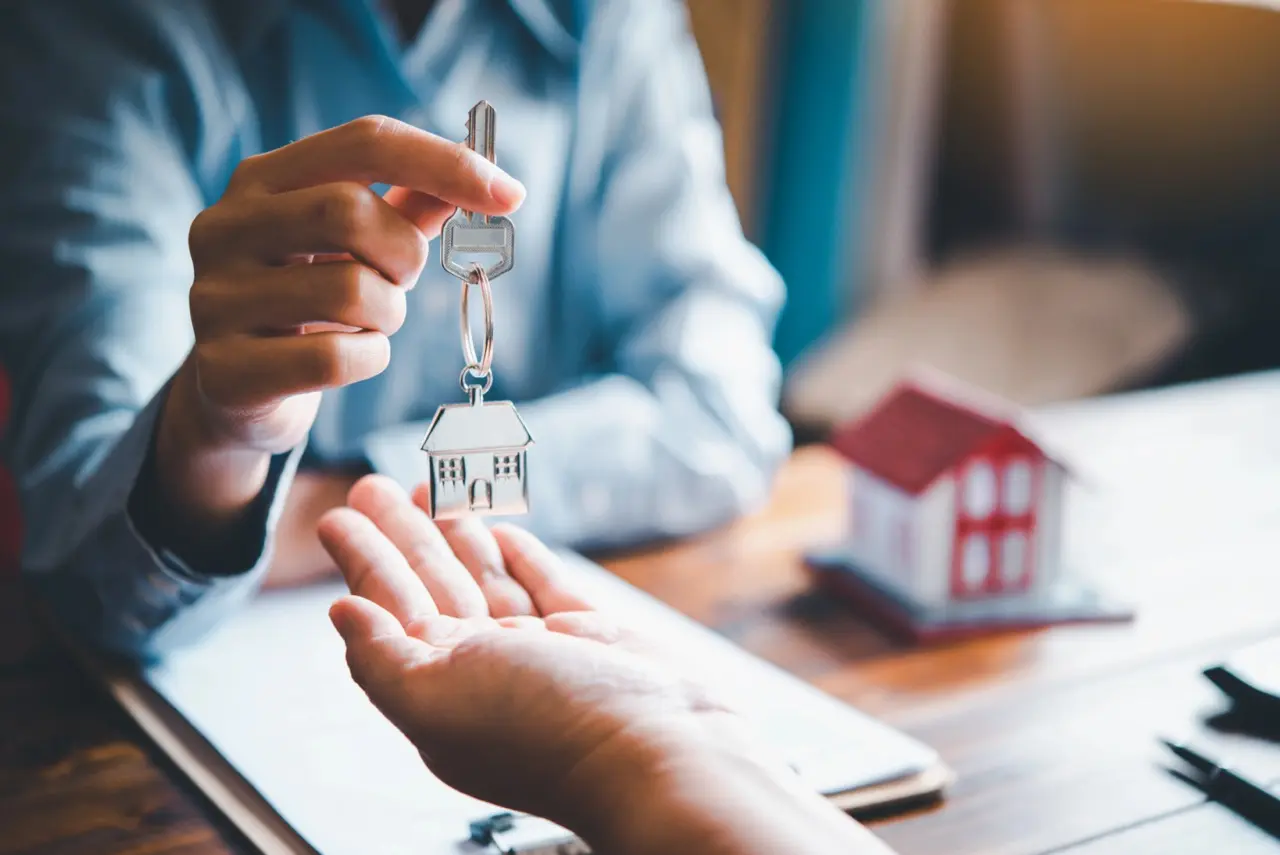 Close-up of landlord handing over house-shaped keychain to new tenant during rental lease signing