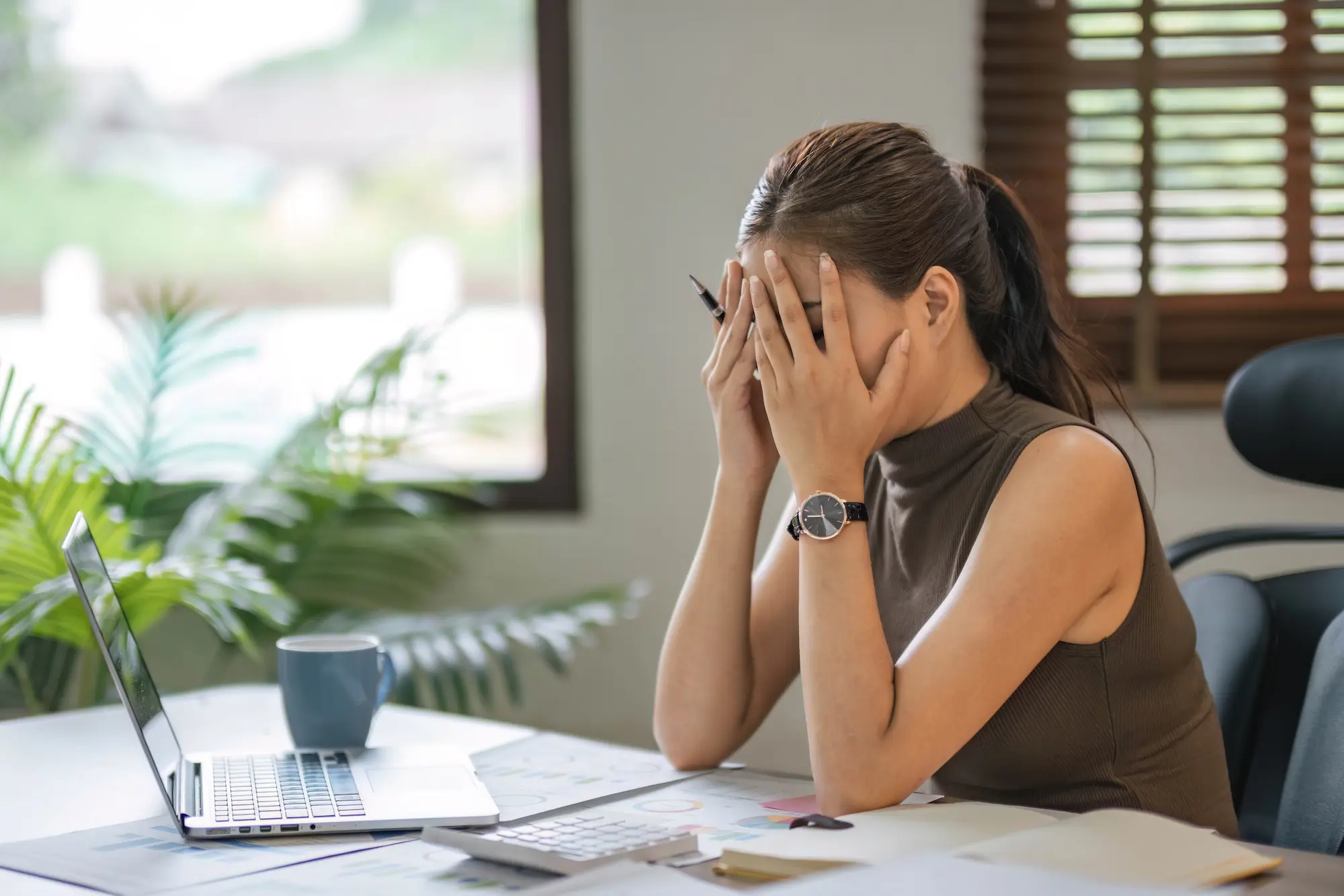 Frustrated landlord covering face at desk with laptop and paperwork, overwhelmed by legal or tenant issues