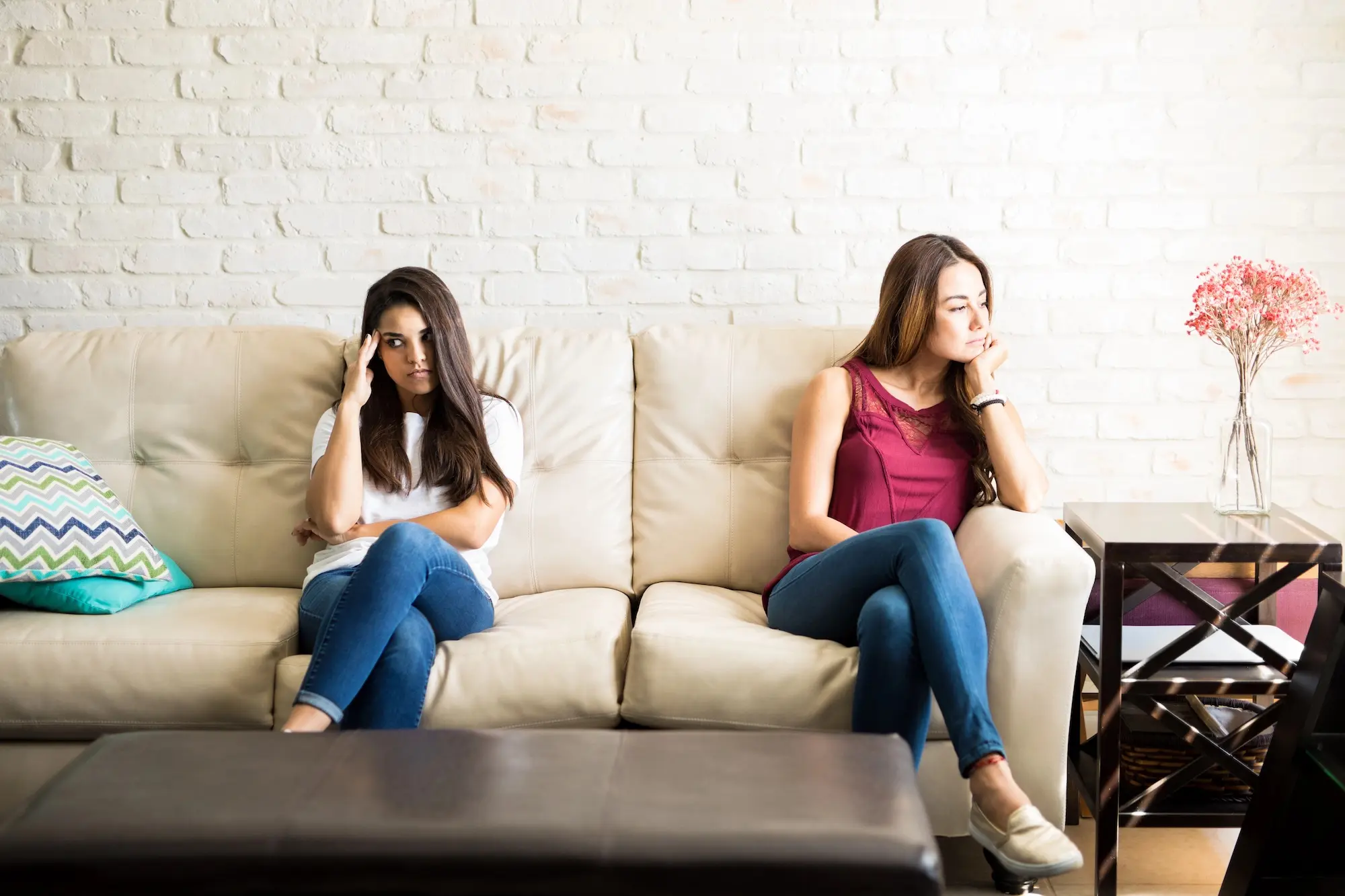 Two frustrated roommates sitting apart on a couch after an argument, facing away from each other