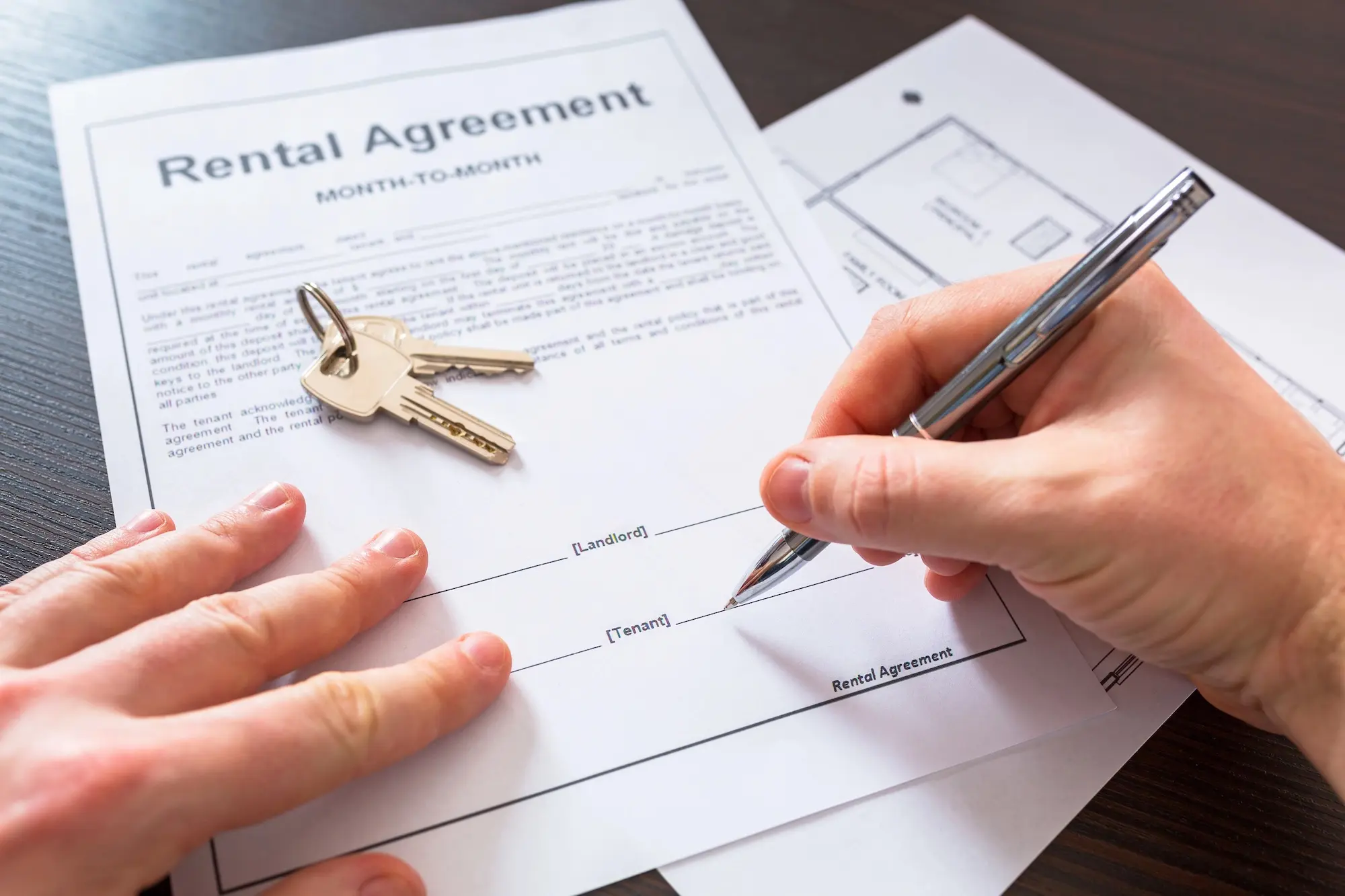 Person signing rental agreement with house keys on the table