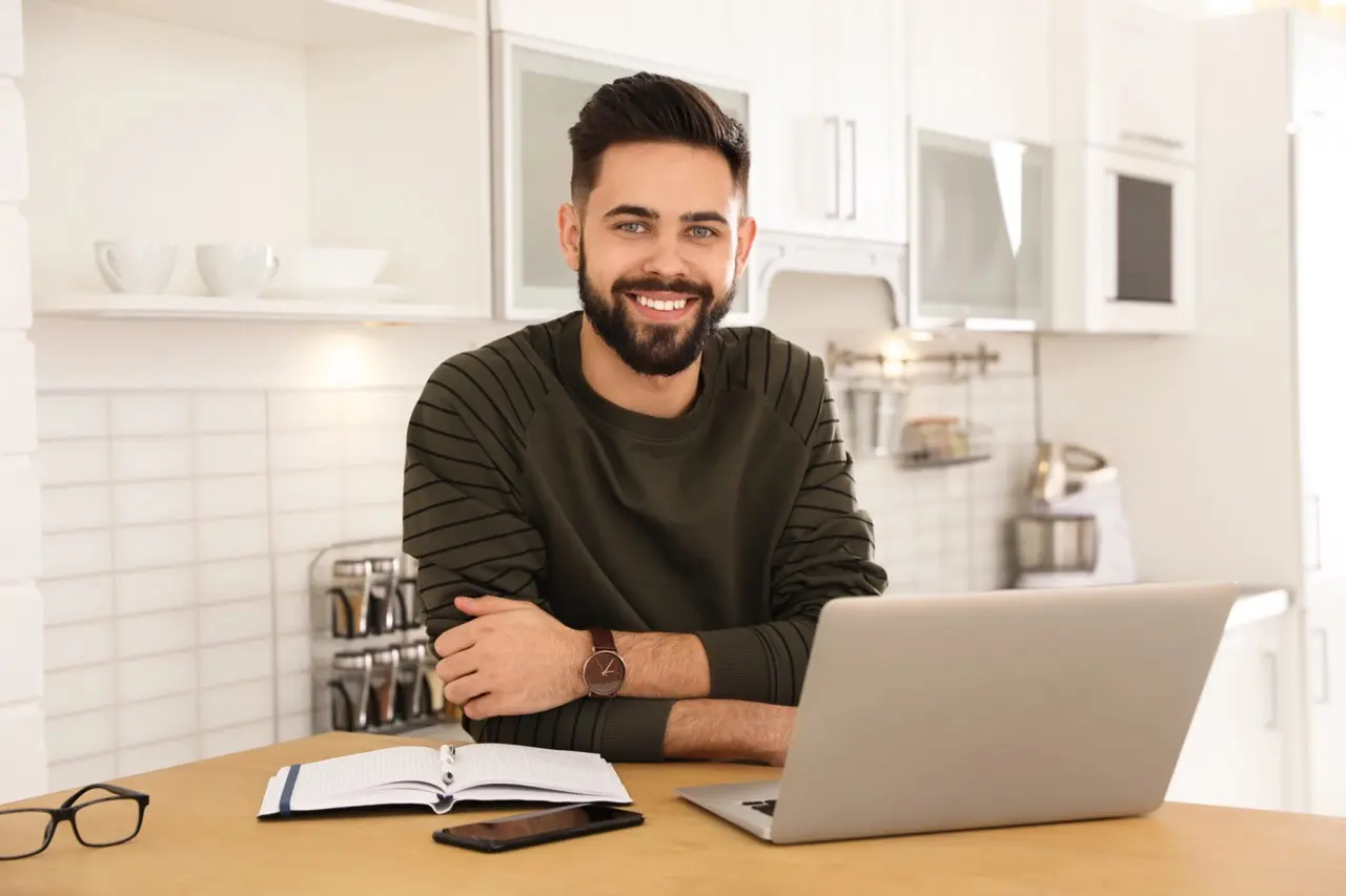 Smiling landlord sitting at kitchen counter with laptop and paperwork, preparing to write a rent increase letter