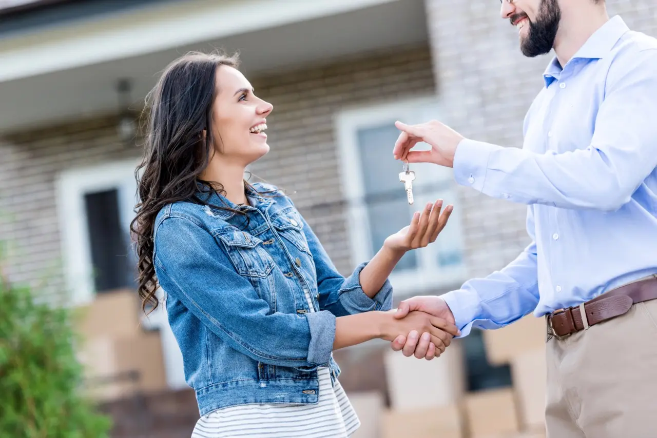 Smiling woman receiving rental keys and shaking hands with landlord outside her new home