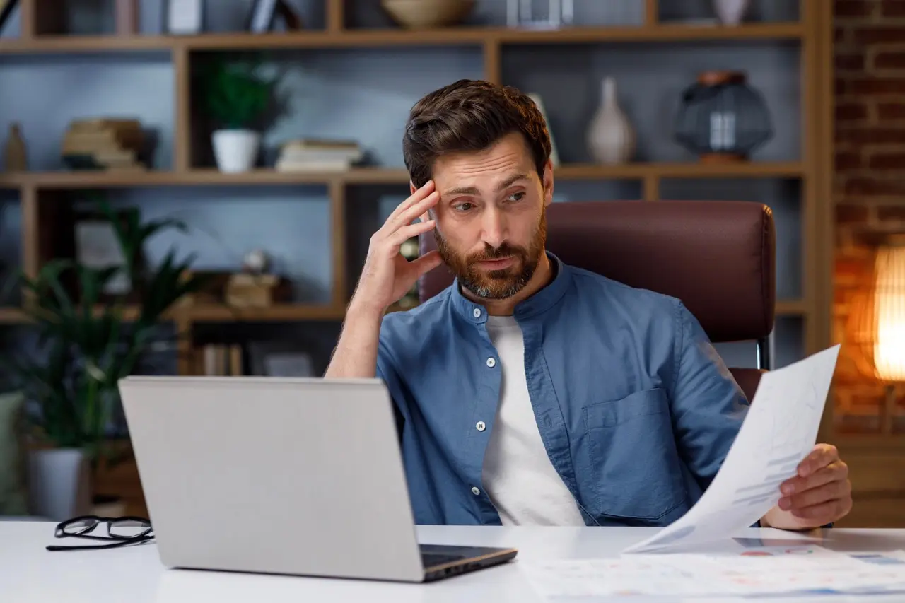 Landlord reviewing rental application paperwork with a concerned expression at his desk