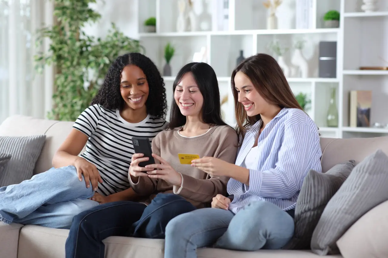 Three roommates discussing shared expenses while using a phone and credit card
