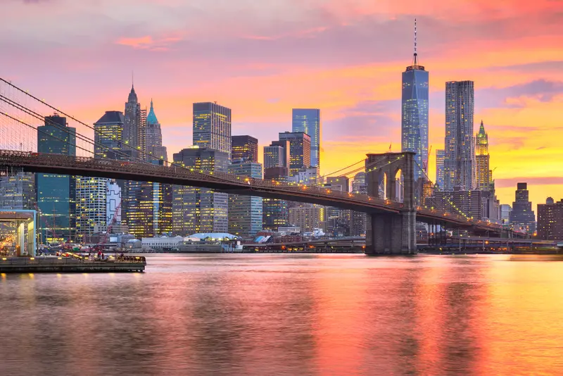 Brooklyn Bridge spanning the East River with One World Trade Center and the Lower Manhattan skyline at sunset